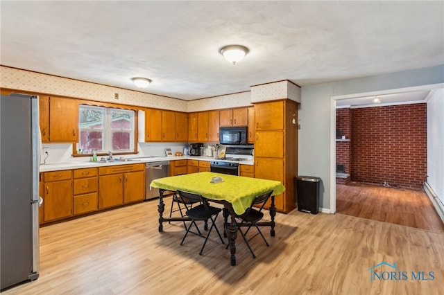 kitchen with appliances with stainless steel finishes, sink, light hardwood / wood-style flooring, and brick wall