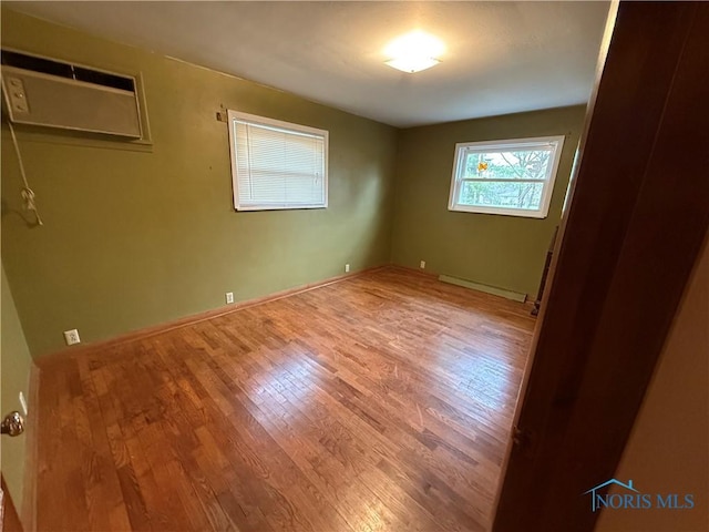 unfurnished room with hardwood / wood-style flooring, a baseboard radiator, and a wall unit AC