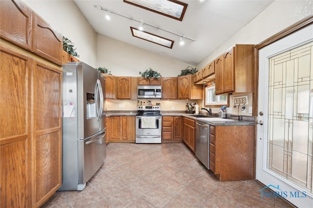 kitchen with appliances with stainless steel finishes, track lighting, lofted ceiling, and sink