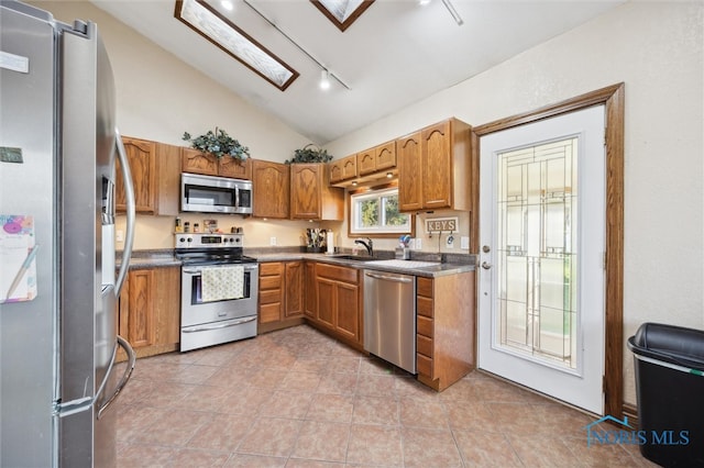 kitchen featuring lofted ceiling, track lighting, sink, light tile patterned floors, and appliances with stainless steel finishes