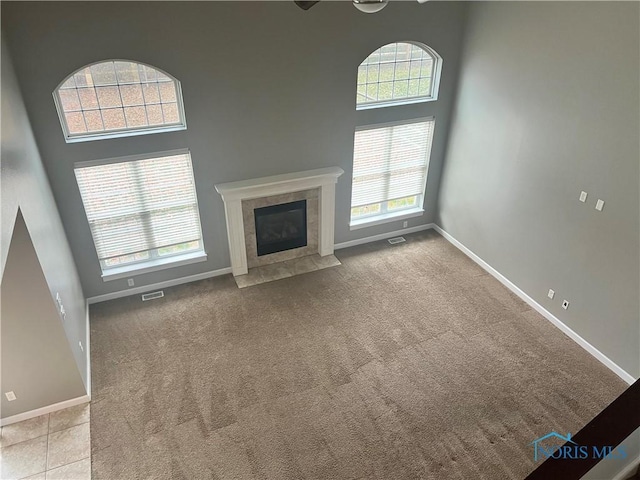 unfurnished living room featuring a towering ceiling, light colored carpet, and plenty of natural light