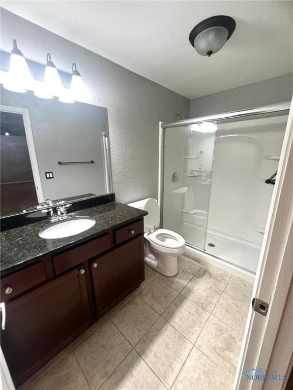 bathroom featuring a shower with door, vanity, tile patterned floors, and toilet