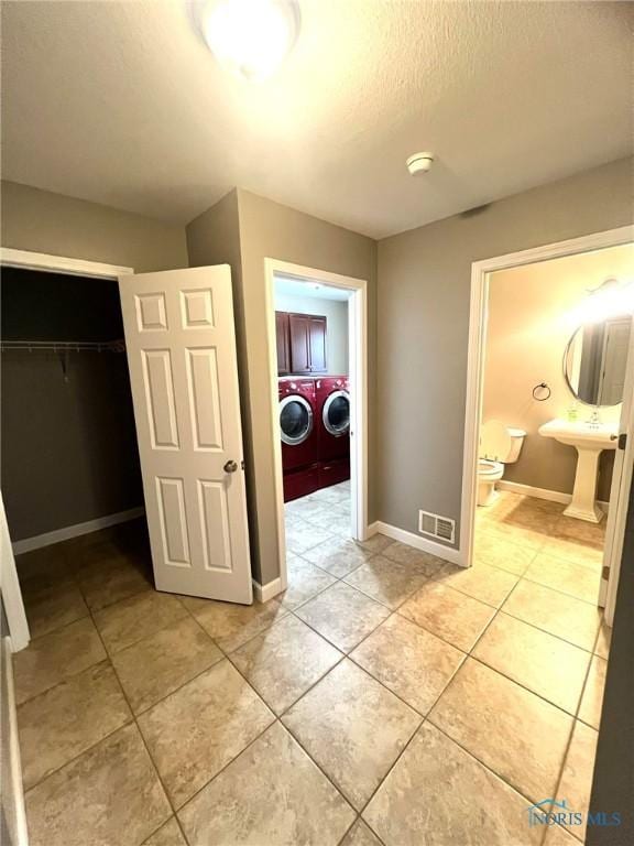 hallway featuring light tile patterned floors, a textured ceiling, sink, and washing machine and clothes dryer