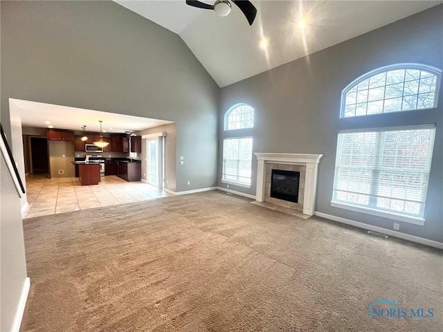 unfurnished living room with a tiled fireplace, high vaulted ceiling, light carpet, and ceiling fan