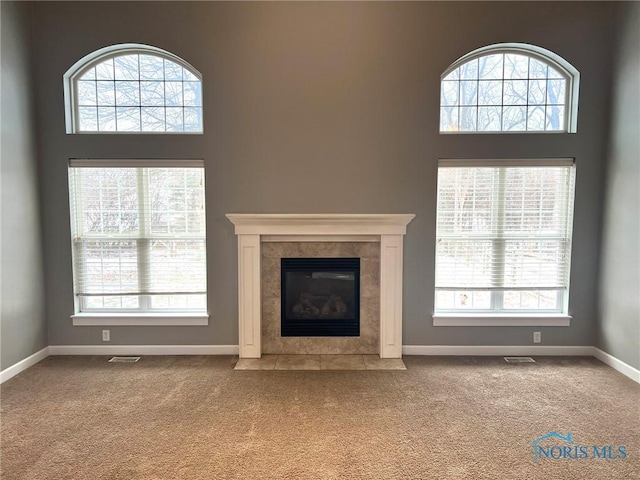 unfurnished living room with carpet floors, a tiled fireplace, and plenty of natural light