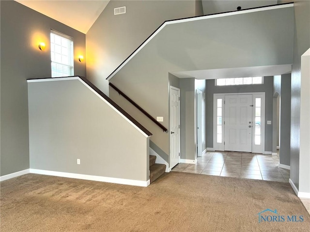 foyer featuring light carpet, high vaulted ceiling, and a healthy amount of sunlight