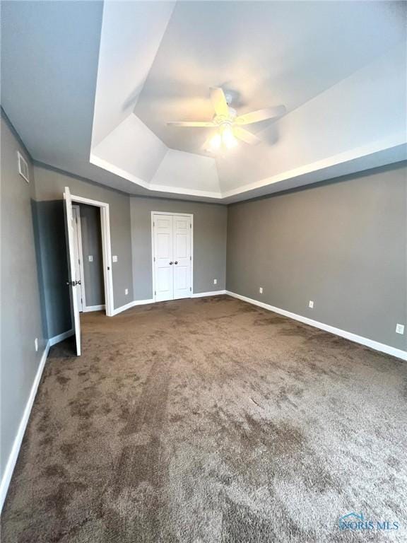 unfurnished bedroom featuring dark carpet, a tray ceiling, a closet, and ceiling fan