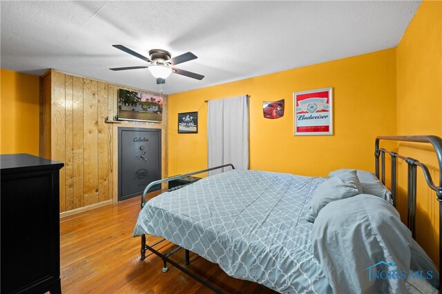 bedroom featuring hardwood / wood-style floors, ceiling fan, a textured ceiling, and wooden walls