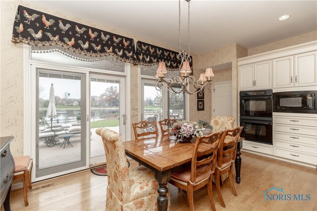 dining space featuring a water view, light wood-type flooring, and a chandelier