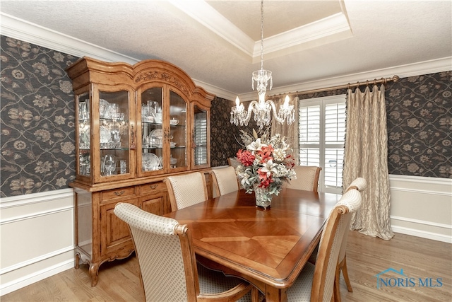 dining room featuring a raised ceiling, a chandelier, ornamental molding, and hardwood / wood-style flooring