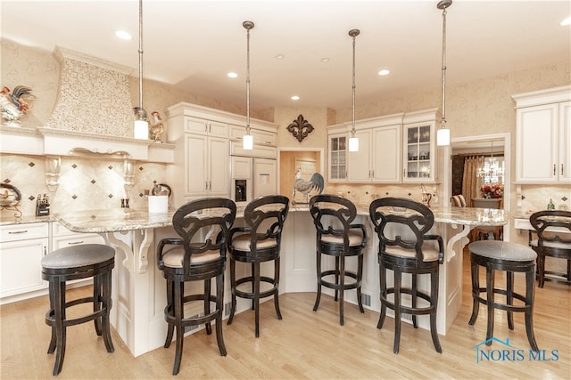 kitchen featuring a breakfast bar area, light hardwood / wood-style flooring, paneled built in refrigerator, and decorative light fixtures