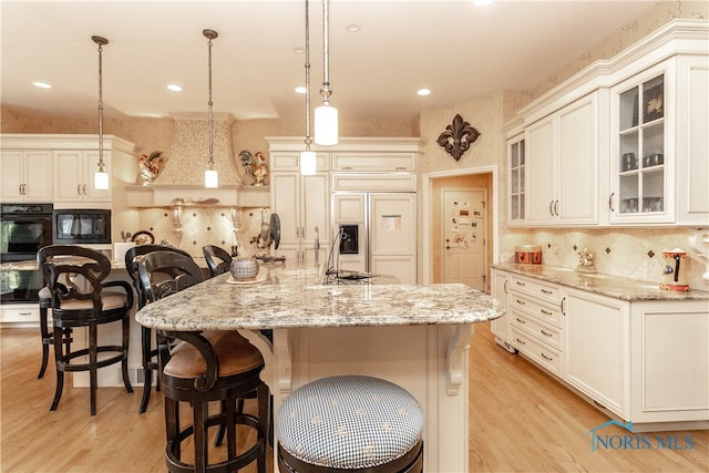 kitchen featuring a center island with sink, hanging light fixtures, light hardwood / wood-style floors, and black appliances