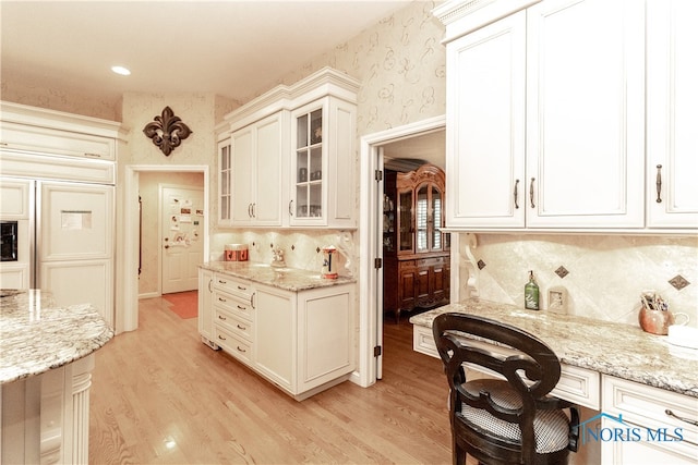 kitchen featuring white cabinets, light stone counters, backsplash, and light hardwood / wood-style flooring