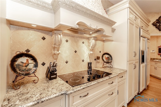 kitchen with black electric cooktop, light stone countertops, light hardwood / wood-style flooring, and cream cabinets