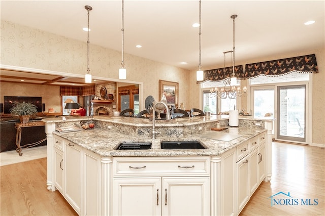 kitchen featuring light stone countertops, sink, a large island with sink, light hardwood / wood-style flooring, and hanging light fixtures