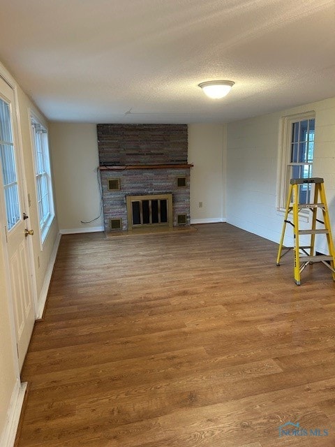 unfurnished living room with wood-type flooring, a textured ceiling, and a brick fireplace