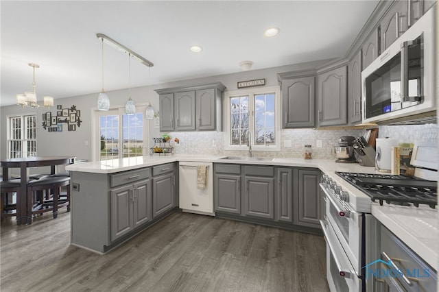 kitchen featuring white dishwasher, sink, hanging light fixtures, gas stove, and dark hardwood / wood-style flooring