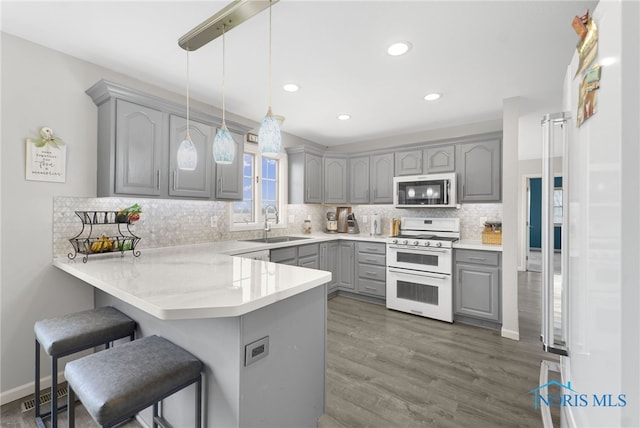 kitchen featuring gray cabinetry, white range, sink, decorative light fixtures, and kitchen peninsula