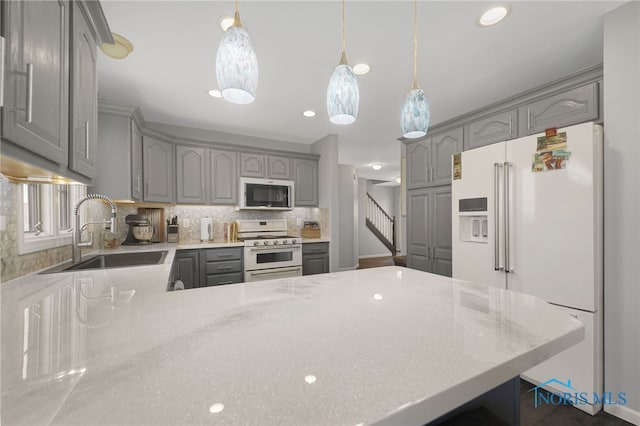 kitchen with backsplash, white appliances, sink, gray cabinets, and hanging light fixtures