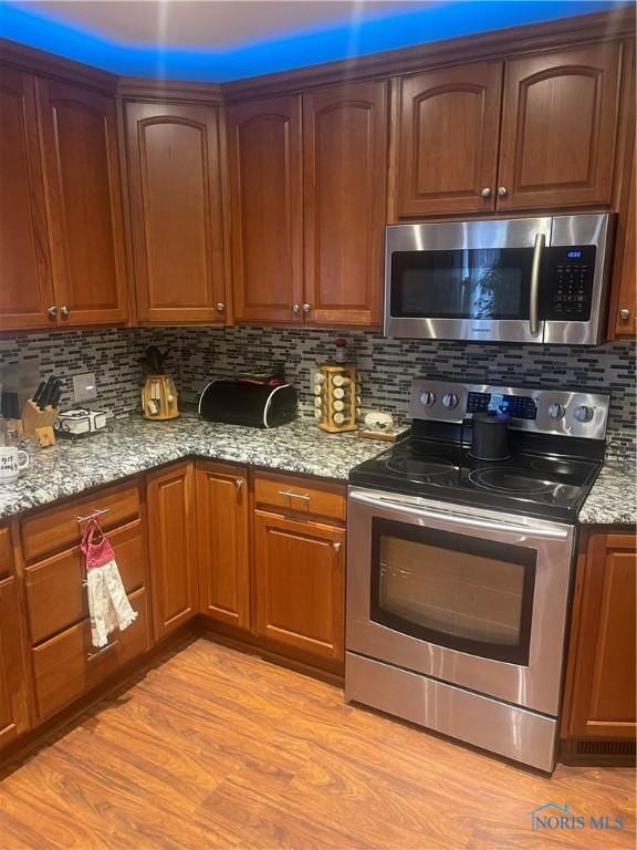 kitchen featuring light stone countertops, light wood-type flooring, stainless steel appliances, and tasteful backsplash