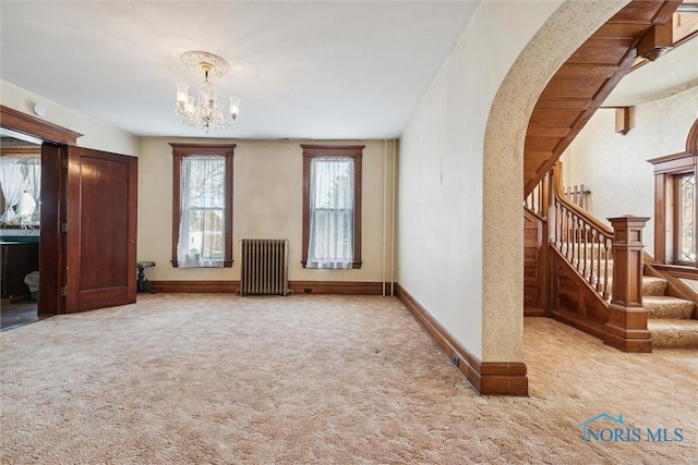 unfurnished living room featuring carpet flooring, radiator heating unit, and a notable chandelier