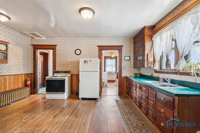 kitchen with wood walls, sink, white appliances, and hardwood / wood-style flooring