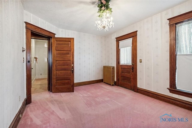 carpeted empty room featuring radiator heating unit, a textured ceiling, and a notable chandelier