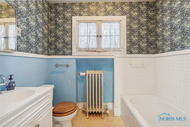 bathroom featuring radiator, a washtub, vanity, tile walls, and toilet