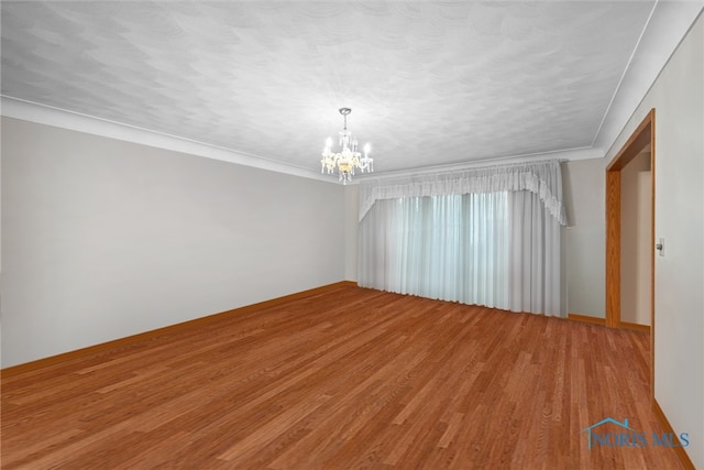 empty room featuring ornamental molding, a notable chandelier, and hardwood / wood-style flooring