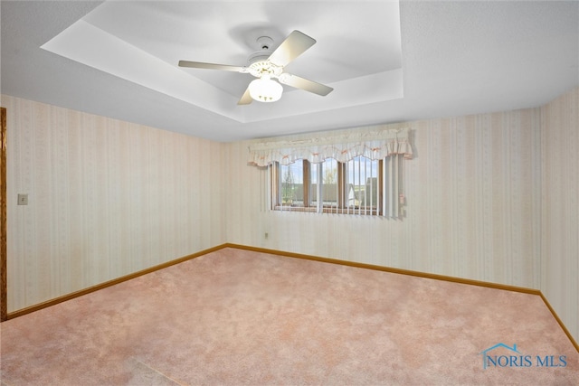 carpeted empty room with ceiling fan and a raised ceiling