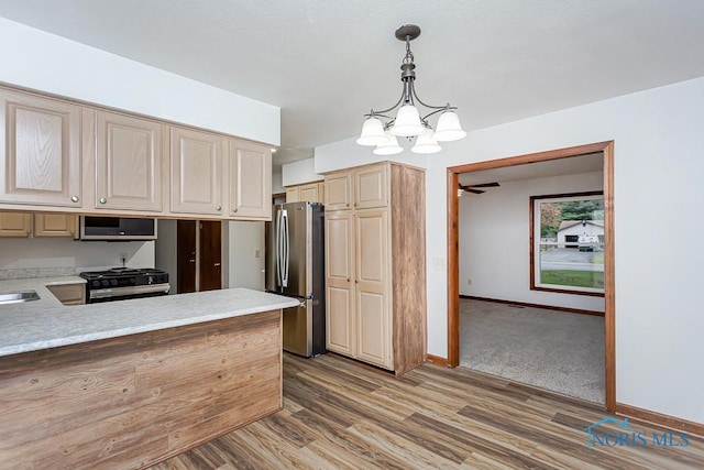 kitchen featuring ceiling fan with notable chandelier, stainless steel appliances, decorative light fixtures, and wood-type flooring