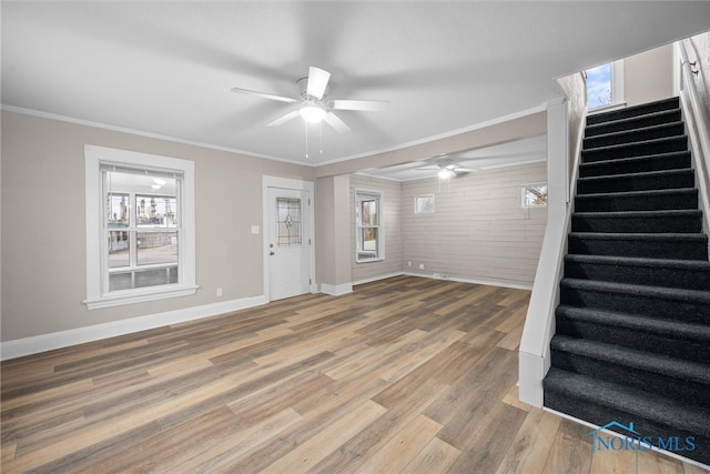 unfurnished living room featuring ceiling fan, wood-type flooring, ornamental molding, and brick wall