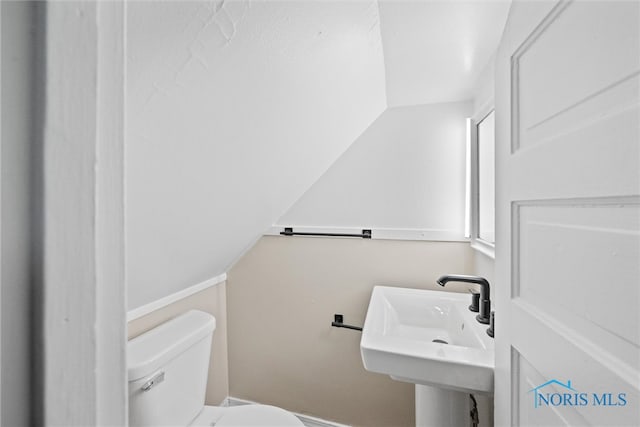 bathroom with toilet, sink, and vaulted ceiling