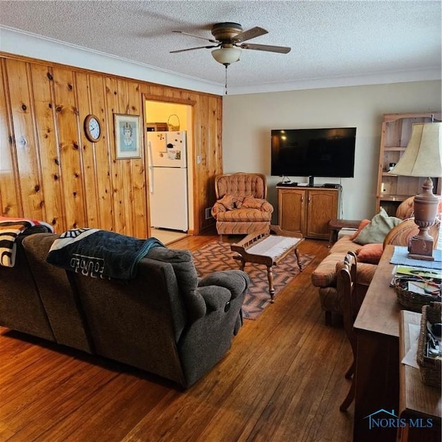 living room featuring hardwood / wood-style floors, crown molding, wooden walls, ceiling fan, and a textured ceiling