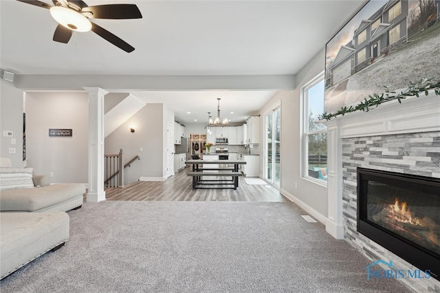 carpeted living room featuring ceiling fan with notable chandelier and a fireplace