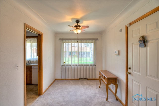 carpeted foyer entrance with ceiling fan, a healthy amount of sunlight, crown molding, and sink