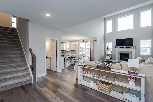 living room featuring a stone fireplace, a towering ceiling, a healthy amount of sunlight, and dark hardwood / wood-style floors