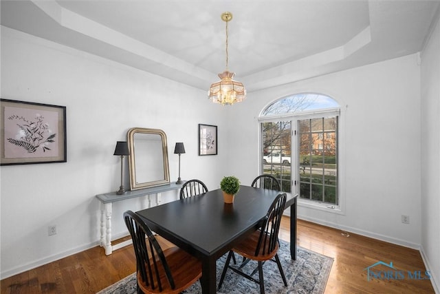 dining space with dark hardwood / wood-style floors, a chandelier, and a tray ceiling