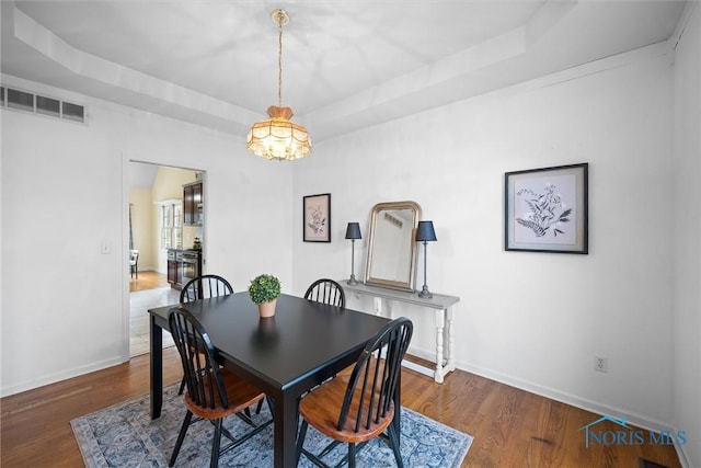 dining area with an inviting chandelier, dark hardwood / wood-style floors, and a raised ceiling