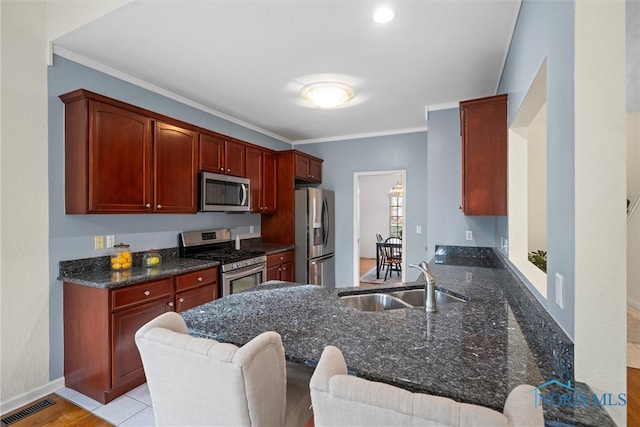 kitchen featuring sink, dark stone countertops, appliances with stainless steel finishes, light hardwood / wood-style floors, and kitchen peninsula