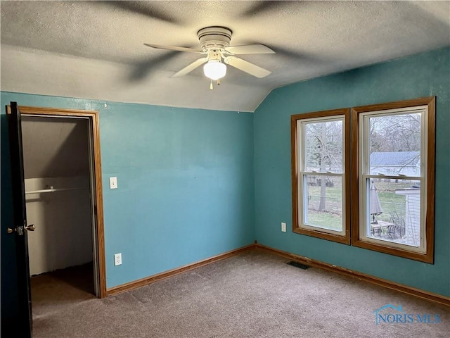 unfurnished bedroom featuring carpet, a textured ceiling, vaulted ceiling, ceiling fan, and a closet