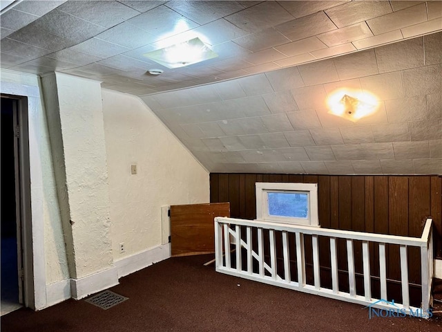 bonus room featuring dark colored carpet, wooden walls, and lofted ceiling