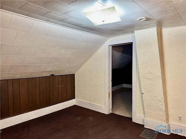 bonus room featuring dark colored carpet, wooden walls, and vaulted ceiling