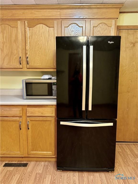 kitchen featuring black fridge, light brown cabinetry, and light wood-type flooring