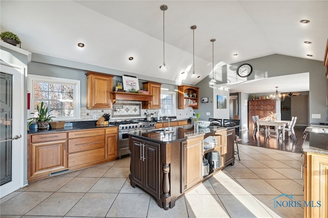 kitchen featuring custom exhaust hood, high end stove, decorative light fixtures, lofted ceiling, and an island with sink