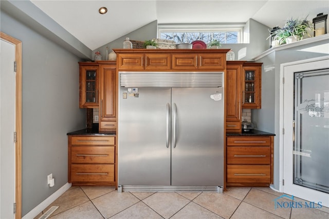 kitchen with dark stone countertops, lofted ceiling, light tile patterned floors, and stainless steel built in refrigerator