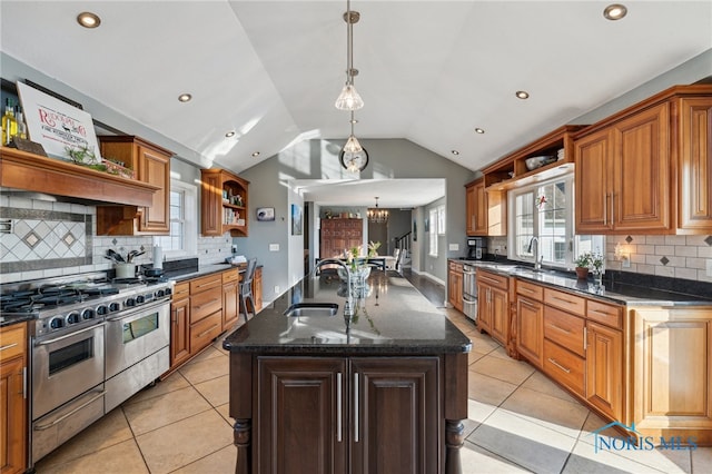 kitchen featuring double oven range, a kitchen island with sink, hanging light fixtures, sink, and vaulted ceiling