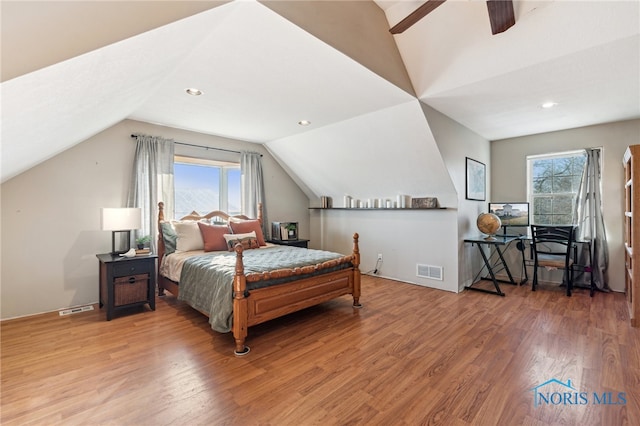 bedroom with multiple windows, ceiling fan, wood-type flooring, and vaulted ceiling