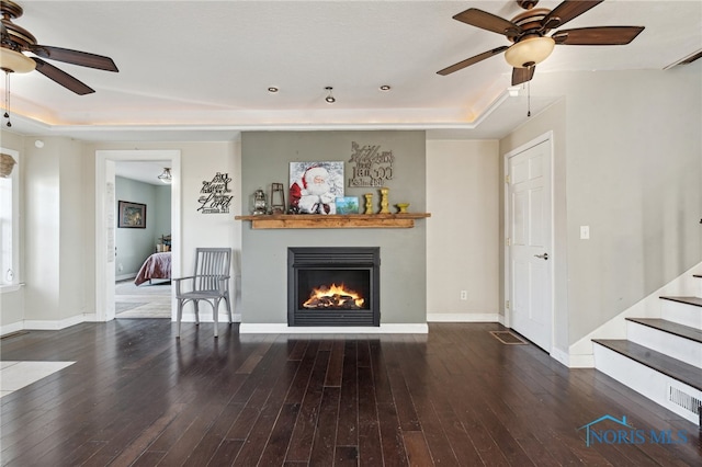 living room with dark hardwood / wood-style floors, ceiling fan, and a raised ceiling