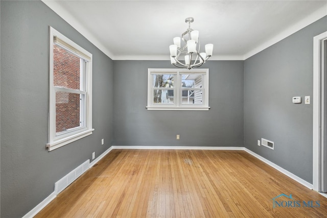 empty room featuring a notable chandelier, a healthy amount of sunlight, and light hardwood / wood-style floors